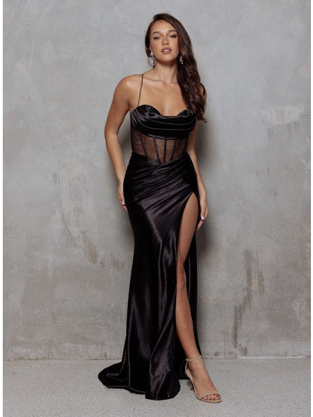 Woman wearing a black satin evening gown with a high slit against a gray background